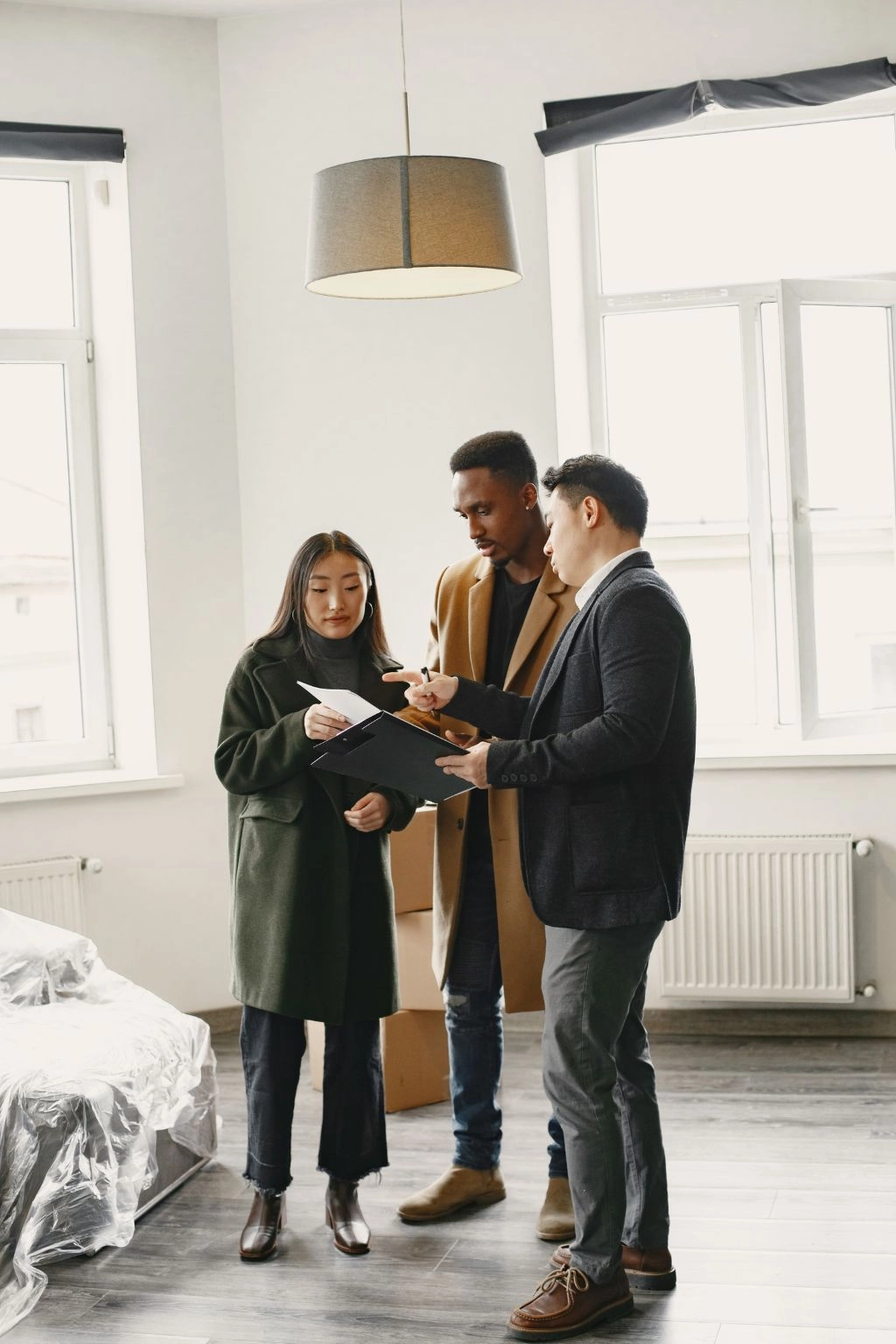Three people standing in an empty apartment reviewing documents together.