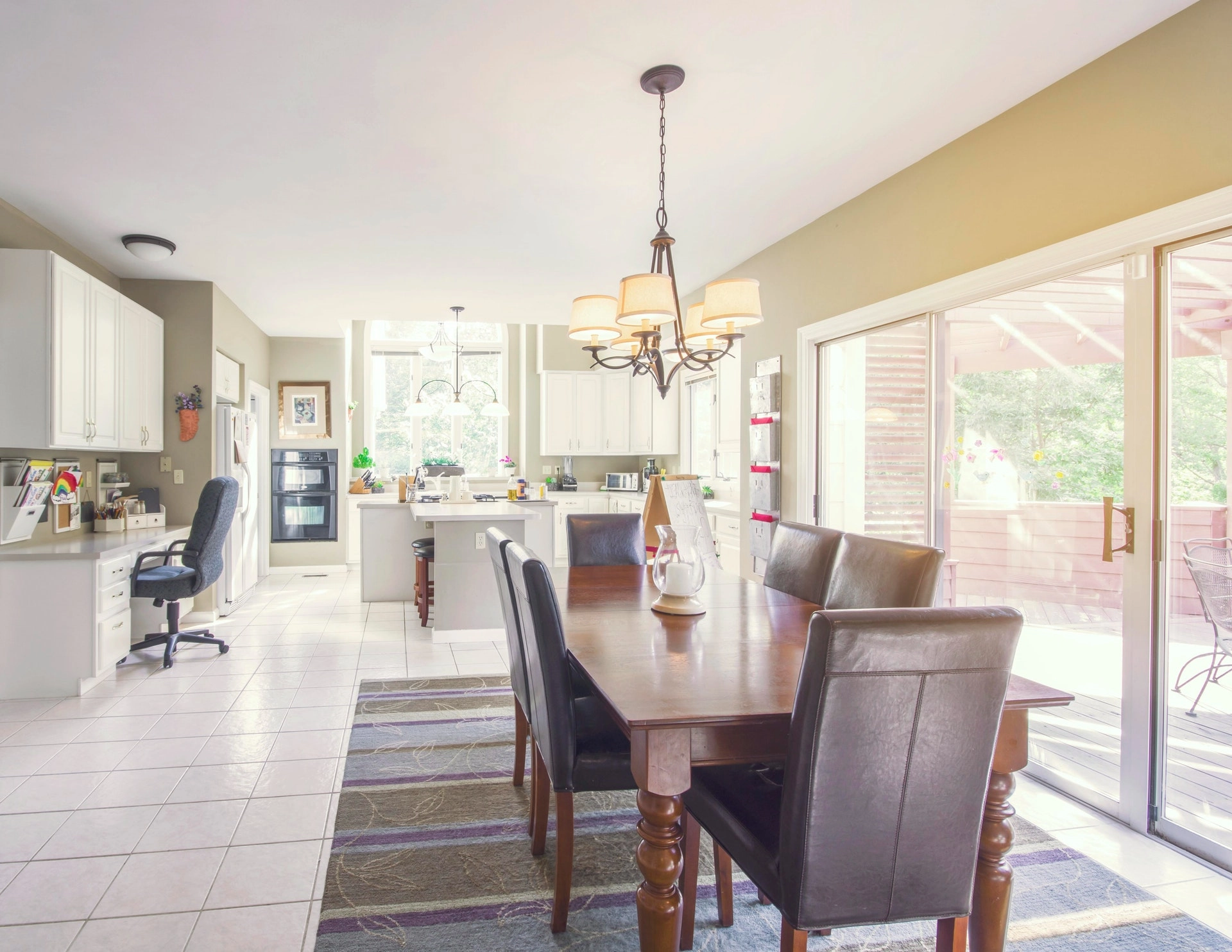 Open-concept dining area with wooden table, leather chairs, and adjacent white kitchen.